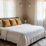 Neatly made bed with white bedding and gold pillows in a bright bedroom.