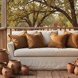 Beige sofa with brown cushions on a wooden deck with trees in the background
