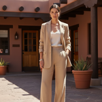 Woman in a beige suit standing in front of a building with potted plants.