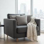 Gray sofa with a white blanket in a room with large windows showing a cityscape.