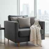 Gray sofa with a white blanket in a room with large windows showing a cityscape.