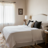 Neatly made bed with white bedding and decorative pillows in a bedroom setting.