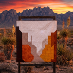 Abstract art piece in a desert landscape with mountains and sunset.
