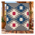A large woven throw blanket with a Southwestern geometric pattern is draped over a rustic wooden porch. The blanket features a gray background with navy blue, cream, and red geometric motifs.