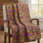 Colorful floral-patterned blanket draped over a wooden chair in a room with a window.