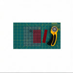 Quilting tools including a rotary cutter, clear ruler, and red square on a green cutting mat.