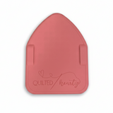 A pink silicone mat with the brand 'Quilted Heartz' embossed on it, placed on a black and white polka dot background.