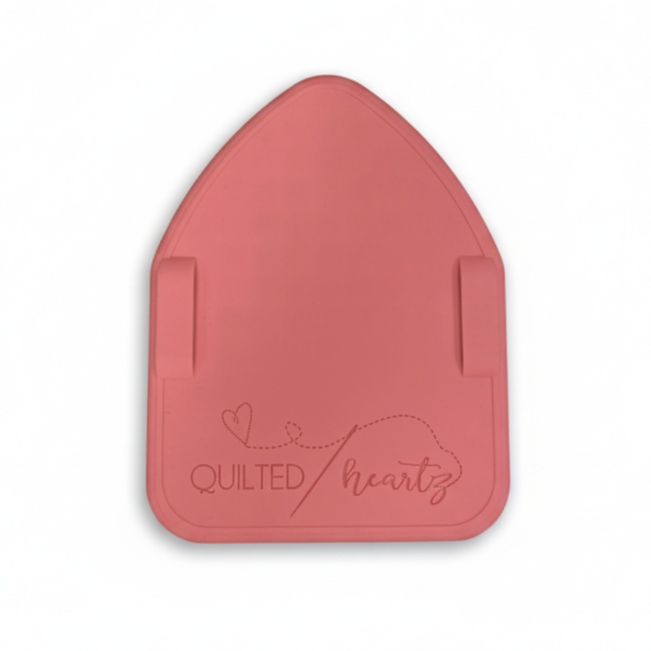 A pink silicone mat with the brand 'Quilted Heartz' embossed on it, placed on a black and white polka dot background.