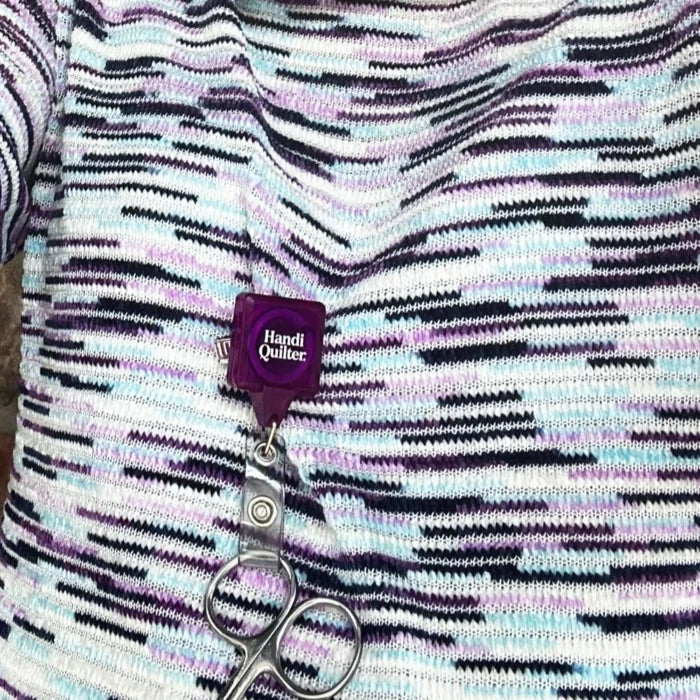 Scissors attached to a purple 'Handi Quilter' lanyard on a patterned fabric background